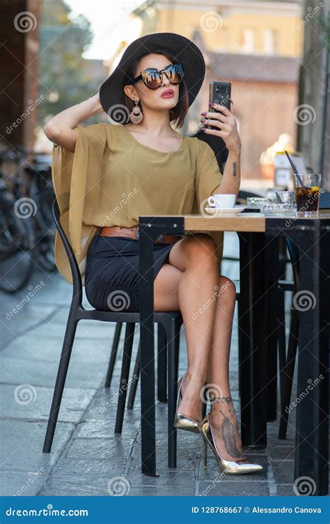 Elegant Italian Woman With Hat And Glasses Checks Her Makeup On Her Smartphone Stock Image