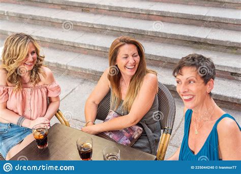 Three Adult Women In A Cafe Outside Laughing And Having Drinks Stock