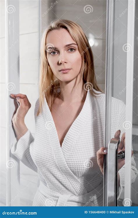 attractive middle age blond woman in white bathrobe in bathroom he enters the glass shower and
