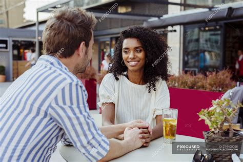 Romantic Multiracial Couple Holding Hands And Looking At Each Other While Sitting At Table In