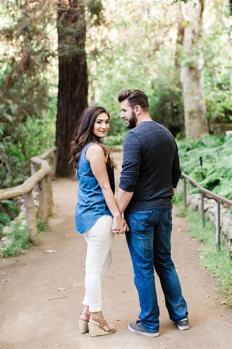 An Engaged Couple Holding Hands While Standing On A Path In The Woods