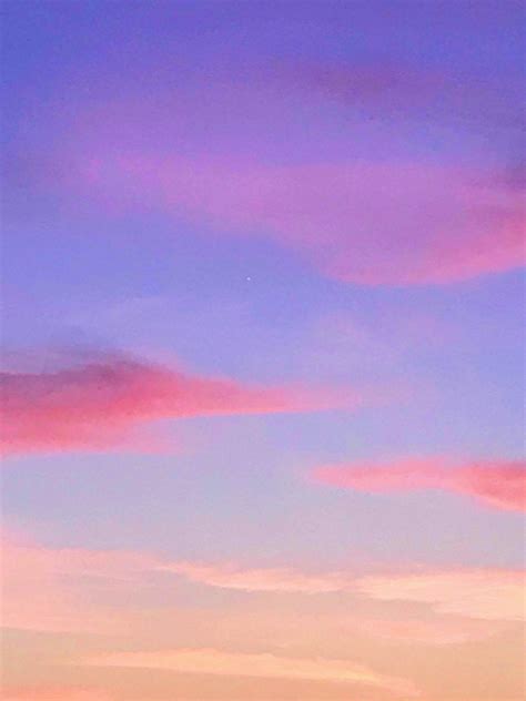 The Airplane Is Flying High In The Sky With Pink And Blue Clouds Above