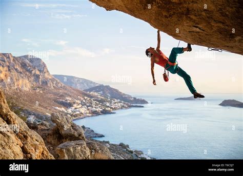 Male Rock Climber Hanging On Cliff With One Hand While Climbing In Cave