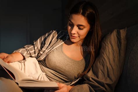 Charming Focused Woman Reading Book While Lying In Bed At Home Stock