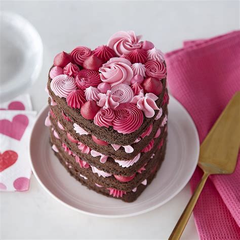 A Heart Shaped Chocolate Cake With Pink Frosting On A Plate Next To A Knife And Fork
