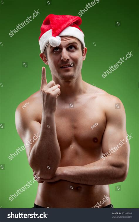 Shirtless Muscular Man Wearing Santa Hat Pointing Upwards Over Green