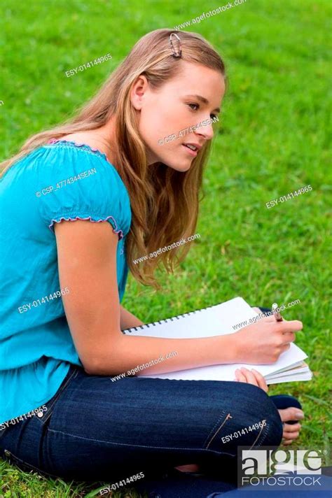 Attractive Young Girl Sitting Down In A Park While Doing Her Home