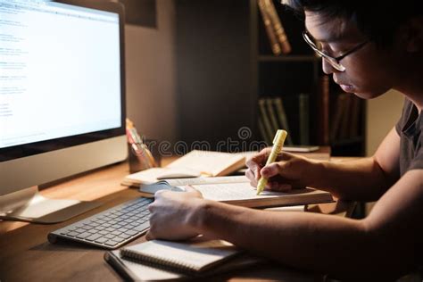 Serious Man Studying With Books And Computer In Dark Room Stock Photo