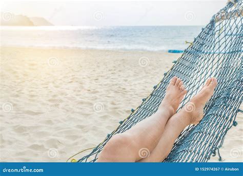 Female Legs Relaxing On Hammock At Sandy Tropical Beach In Summer