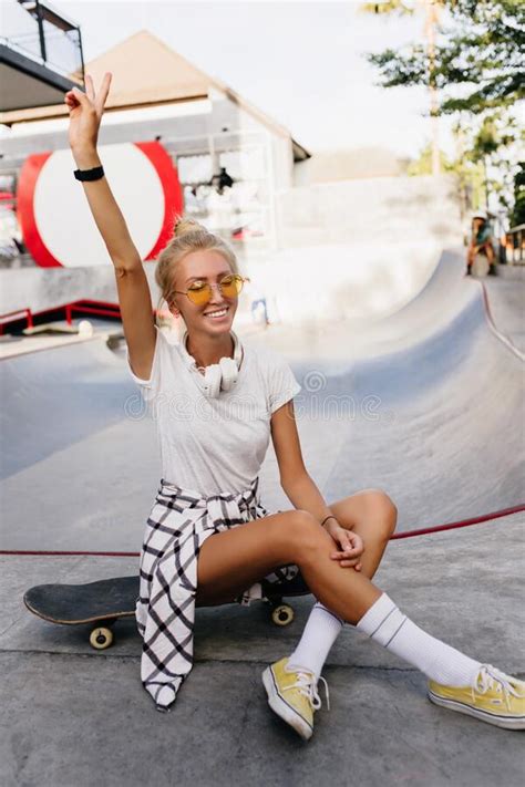 graceful tanned skater girl waving hand during photoshoot cheerful blonde woman in white t