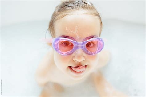 Cute Young Girl With Swim Goggle Sticking Out Her Tongue While Sitting In A Bathtub By Stocksy