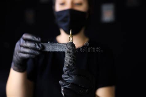 Tattoo Artist In Black Gloves Holds A Tattoo Machine In Front Of Her