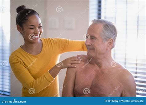 Smiling Female Therapist Giving Neck Massage To Shirtless Senior Male Patient At Hospital Ward