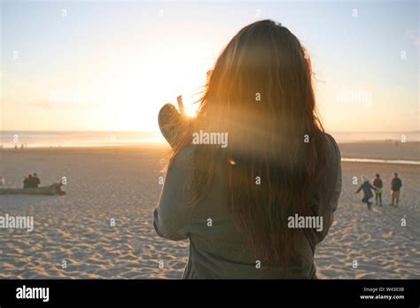 Young Woman With Long Red Hair Takes A Photo At Sunset On The Beach