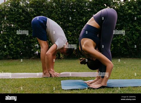 Side View Of Man And Woman Doing Standing Forward Bend On Mats While