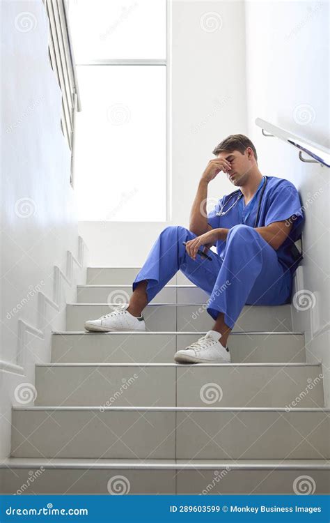 Stressed Male Doctor Or Nurse Wearing Scrubs Sitting On Stairs In