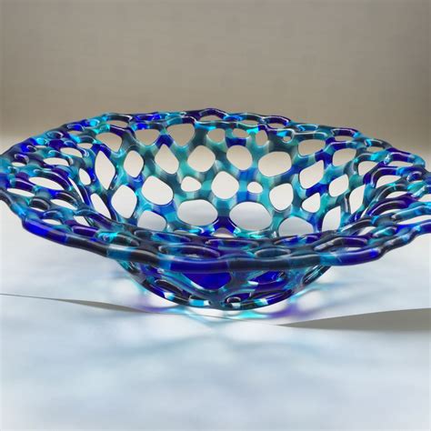 A Blue Glass Bowl Sitting On Top Of A White Table Next To A Black Object