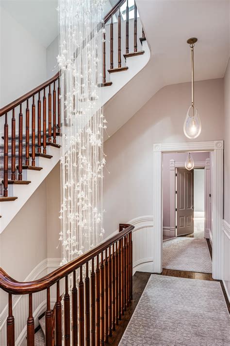 A Double Staircase Features Walnut Banisters And A Glamorous Chandelier