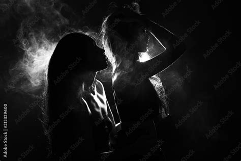 Silhouette Of Two Sexy Woman Kissing Holding In Darkness Through Light