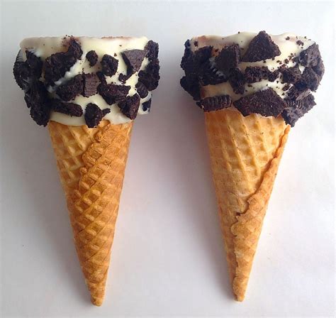 Two Ice Cream Cones With Chocolate Chips And White Icing On Them Sitting Side By Side