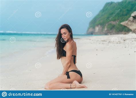 Het Sexy Meisje Met Sportief Lichaam In Zwarte Bikini Stelt Op Strand Met Blauwe Oceaan Bij