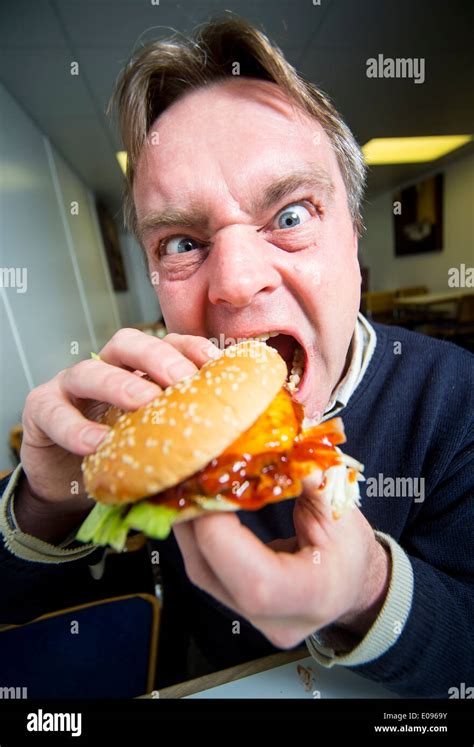 A Man Biting Aggressively Into A Burger Eating A Burger Stock Photo