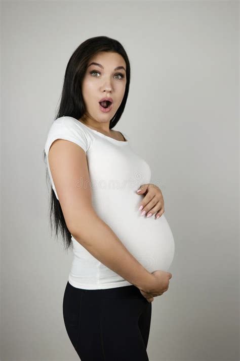 Beautiful Pregnant Brunette Woman Holding Her Pregnant Belly With Surprise On Isolated White