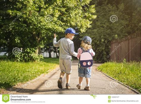Two Young Children Friends Boy And Girl Hold Hands And Walk Along Road