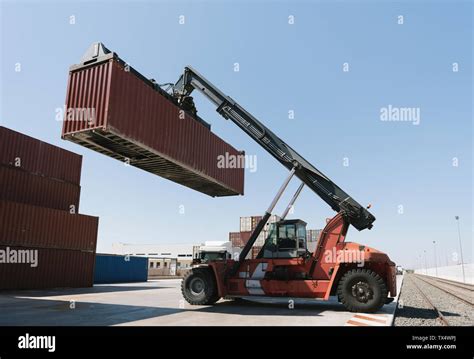 Crane Lifting Cargo Container Near Railway Tracks On Industrial Site