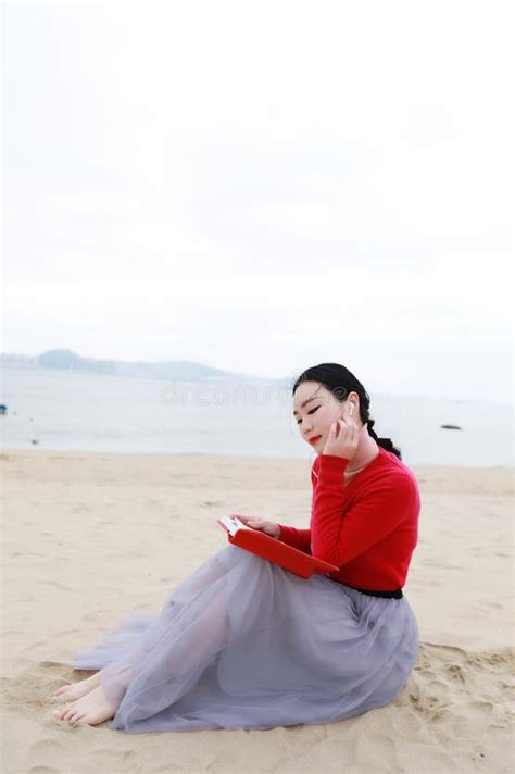 Young Asian Chinese Woman Read Sit On Sand Reading Book At Beach Stock