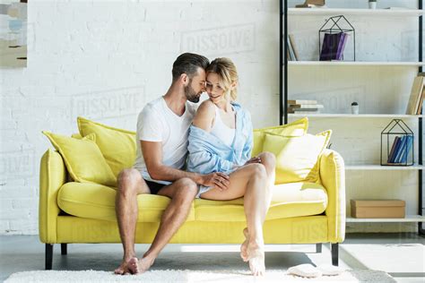 Full Length View Of Young Barefoot Couple In Underwear Sitting Together On Yellow Couch Stock
