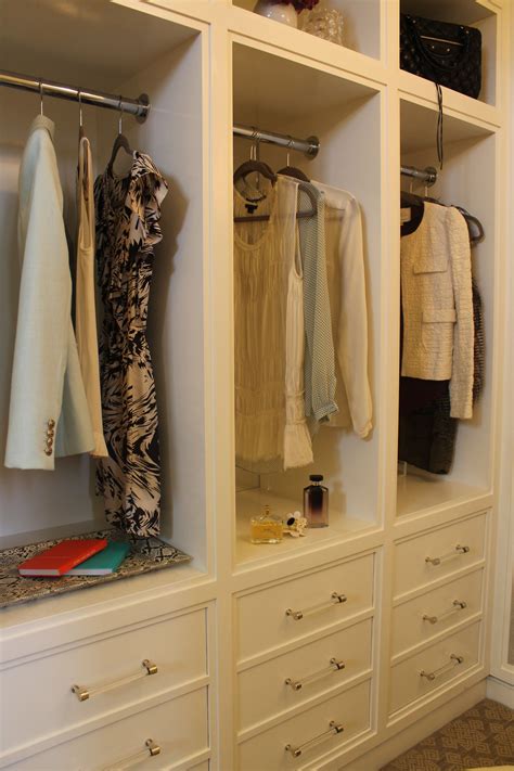 An Organized Closet With White Drawers And Clothes Hanging On The Rails