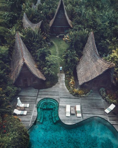 An Aerial View Of A Pool Surrounded By Greenery And Thatched Roof Huts In The Jungle