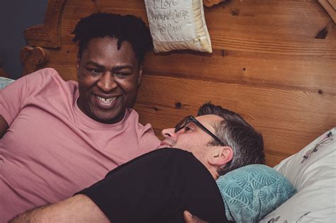 An Interracial Gay Couple Talking Lying Down In Their Bedroom Stock