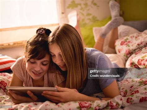 Girl Friends Lying On A Bed Sharing A Digital Tablet High Res Stock