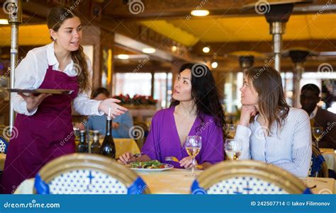 Attentive Young Waitress Talking To Female Guests In Restaurant Stock