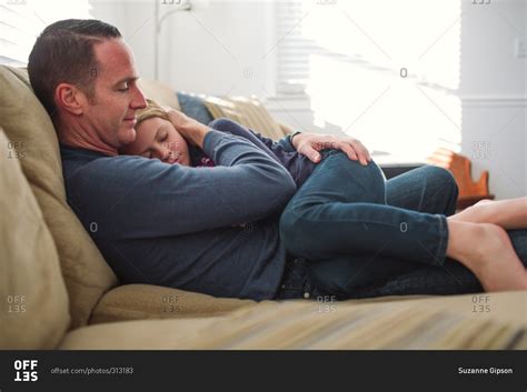 Father Sitting On A Sofa Holding His Sleepy Daughter On His Lap Stock Photo Offset