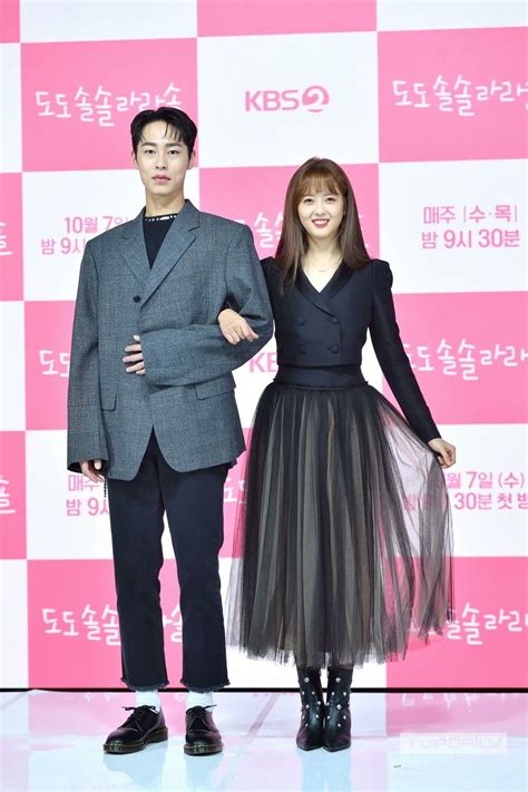 a man and woman standing next to each other in front of a pink wall with korean characters on it