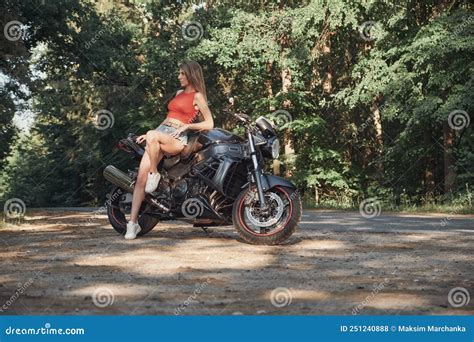 Young Woman Biker Sitting On A Motorcycle On The Side Of A Forest Road