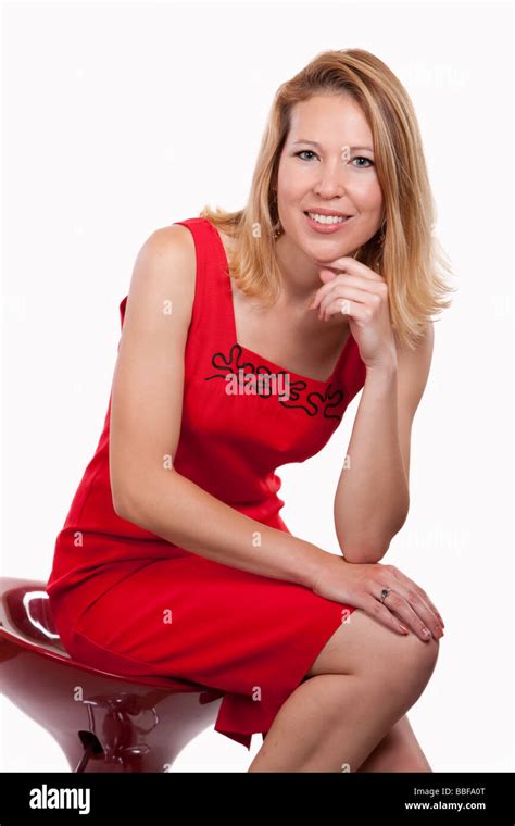 Attractive Blond Woman Wearing Red Dress Sitting On A Stool Over White