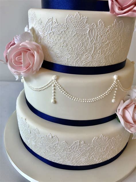 A Three Tiered Wedding Cake With Pink Roses On The Top And Blue Trimmings