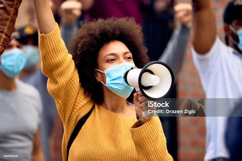 Black Female Activist Wearing Protective Face Mask While Shouting Through Megaphone On A Protest
