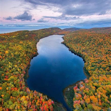 An Aerial View Of A Lake Surrounded By Trees In The Fall With Leaves