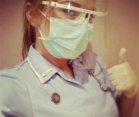 A Woman In Blue Uniform Wearing A Surgical Mask And Holding A