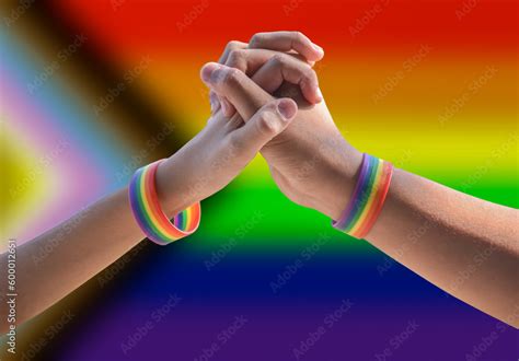 Closeup Hands Of Gay Couple Which Wear Rainbow Wristbands Around With Blurred Lgbtq Flag