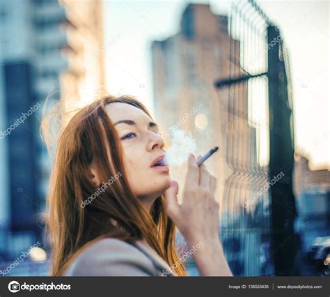 Red Hair Girl Smokes In The Background Of City Outside Stock Photo