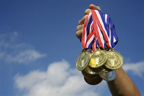 Athlete Hand Holding Up Bunch Of Gold Medals Blue Sky Montessori