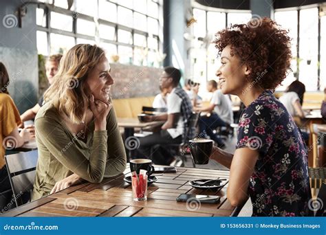 Two Female Friends Meeting Sit At Table In Coffee Shop And Talk Stock