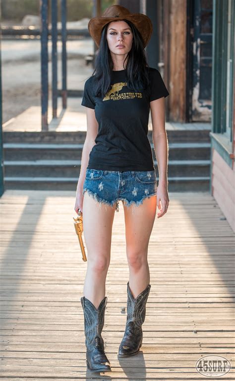 Pretty Cowgirl Model Goddess With Cowboy Hat Cowboy Boots And A Gold Revolver Gun Short