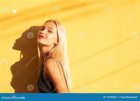 Attractive Tricky Blonde Girl In Black Top Isolated Over Yellowe Wall